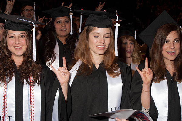 graduating students holding up hook em horns
